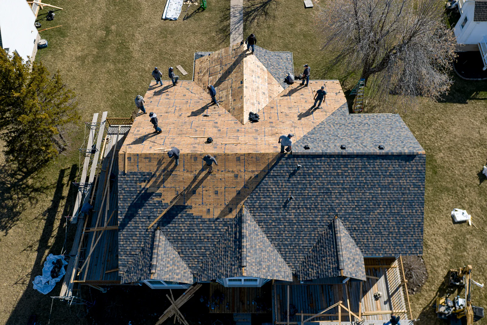 A drone shot captures roofers working across a large multi-gable roof